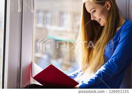 Woman sitting on window sill reading book at home 126951155
