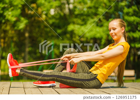 Girl doing exercise outdoor, using resistance fit band. 126951175