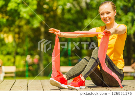 Girl doing exercise outdoor, using resistance fit band. 126951176