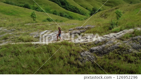 Young woman enjoying a hike in a beautiful green valley, exploring the landscape on a sunny day, promoting sustainable and responsible tourism 126952296