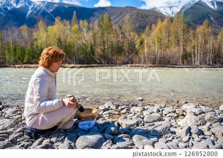 Woman performing a sound ritual with a Tibetan singing bowl by the Altai river. Concept of feminine energy, sacred vibration, and shamanic connection to the Earth 126952800