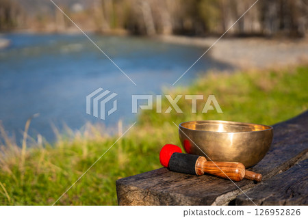 Tibetan singing bowl resting on a wooden bench by the Altai river. Concept of sacred stillness, energy resonance, and spiritual presence in untouched nature. Tibetan singing bowl resting on a wooden bench by the Altai river. Concept of sacred stillness, energy resonance, and spiritual presence in untouched nature. 126952826