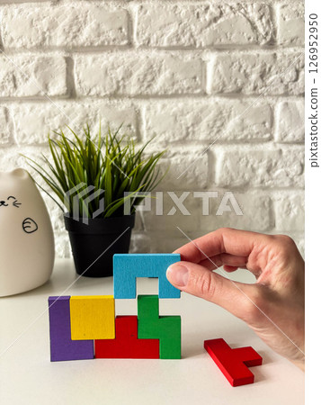 Female hand assembling wooden cube puzzle on white background with potted plant in background. 126952950
