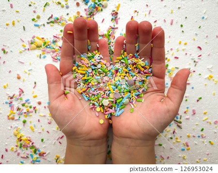 Child's hands are covered with multi-colored sugar sprinkles and form a heart shape. Child plays with small sprinkles topping. Mother's Day. Child's hands are covered with multi-colored sugar sprinkles and form a heart shape. Child plays with small sprinkles topping. Mother's Day. 126953024