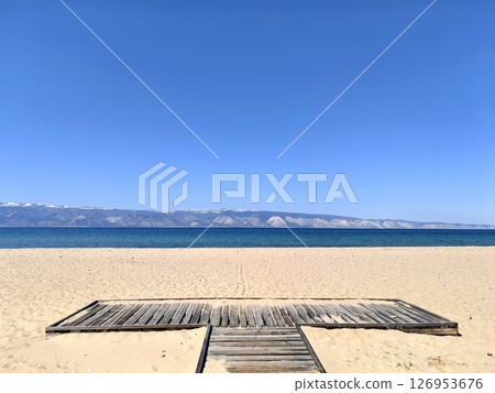 wooden path leading through sandy beach towards calm sea under clear blue sky. closeup. wooden path leading through sandy beach towards calm sea under clear blue sky. closeup. 126953676