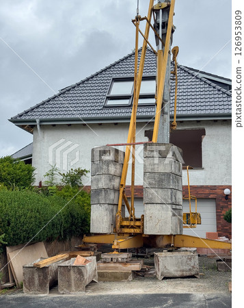 A massive drilling rig positioned in a residential area near a house. The machinery, designed for heavy-duty construction tasks, is central to the urban development context. A massive drilling rig positioned in a residential area near a house. The machinery, designed for heavy-duty construction tasks, is central to the urban development context. 126953809