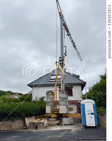 Large construction crane setup near a residential house with a portable restroom nearby. The scene highlights urban development work and infrastructure changes in progress. 126953812