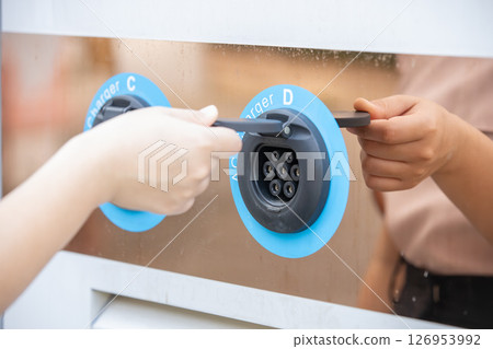 Closeup hand opening electric car charger plug socket at charging dock for charging EV car battery Closeup hand opening electric car charger plug socket at charging dock for charging EV car battery 126953992