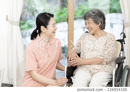 A female caregiver talking to a senior woman in a wheelchair 126954188