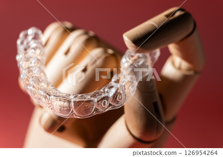 Close-up of wooden elegant hand holding invisible clear aligners, on pastel pink background. Healthy lifestyle and teeth concept 126954264