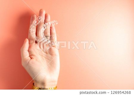 Close up top view female hand holding dental aligner retainer on palm for beautiful dental treatment. Shot indoor in studio on pink background 126954268
