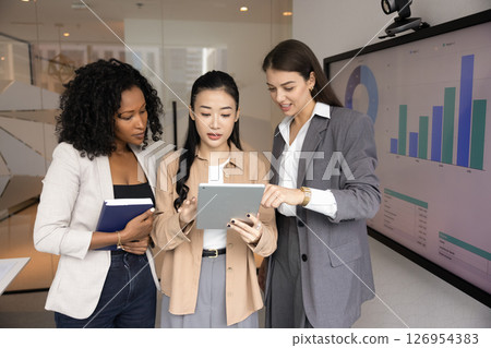 Multiethnic professional women reviewing or discussing digital content on tablet Multiethnic professional women reviewing or discussing digital content on tablet 126954383