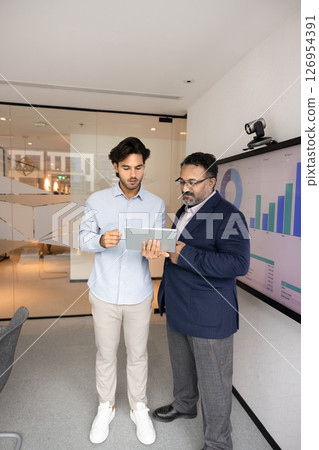 Two multiethnic professionals reviewing financial data or analytics on tablet 126954391