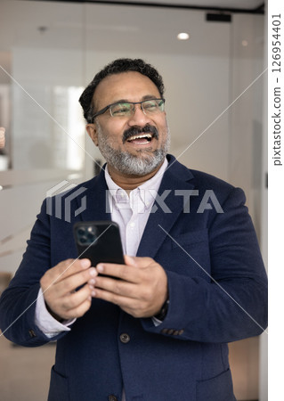 Happy Indian businessman in suit standing in workplace with smartphone 126954401