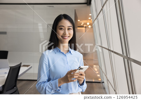 Chinese professional woman standing confidently in modern office with smartphone 126954425