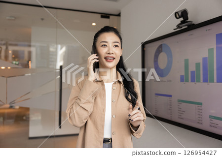 Asian professional woman engaged in phone conversation in modern office Asian professional woman engaged in phone conversation in modern office 126954427