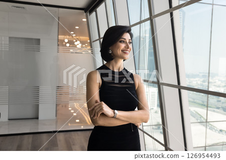 Confident Armenian businesswoman dressed in dress looks out panoramic window 126954493
