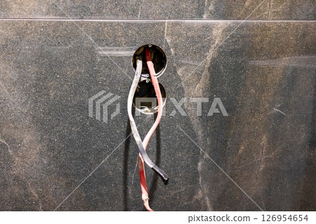 A collection of wires is dangling from an opening in a wall A collection of wires is dangling from an opening in a wall 126954654