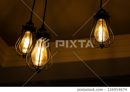 Three bright light bulbs are hanging from the ceiling in a dark room 126954674