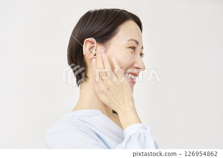 Woman in her 40s using a hearing aid, white background Woman in her 40s using a hearing aid, white background 126954862