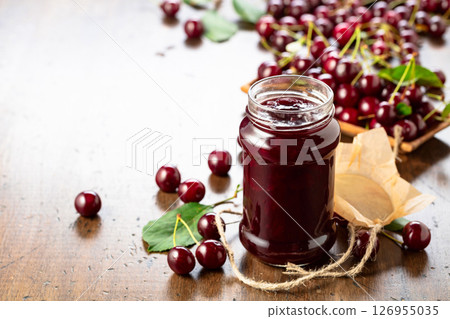 Cherry jam and fresh berries on an old wooden table. Cherry jam and fresh berries on an old wooden table. 126955035