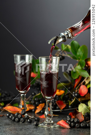 Black chokeberry drink is poured from a bottle into a glass. 126955042