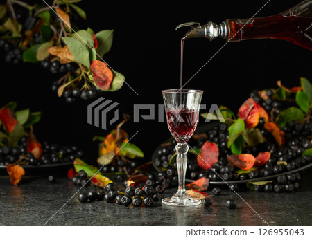 Black chokeberry liqueur and fresh berries on a black stone table. 126955043