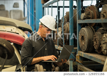 Old used car part warehouse worker checking inventory in garage. Staff worker working in recycle motor junkyard auto parts management. 126955166