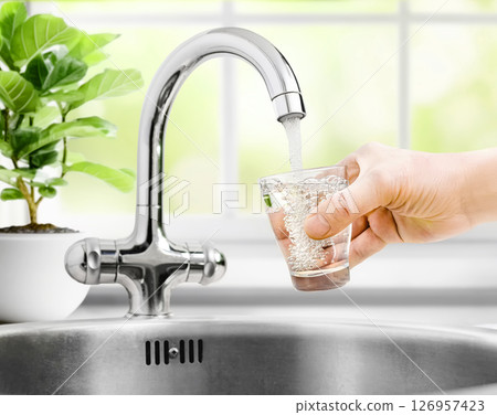 Man pours water from faucet into glass at home 126957423