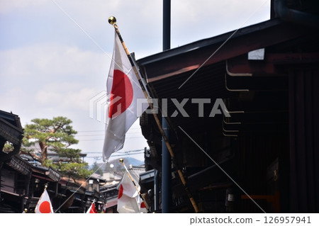 Old townscape of Takayama City, Gifu Prefecture, Japan. Old houses with the Japanese flag flying and beautiful blue sky Old townscape of Takayama City, Gifu Prefecture, Japan. Old houses with the Japanese flag flying and beautiful blue sky 126957941