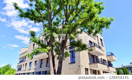 Eco architecture. Green tree and new residential building. Harmony of nature and modernity. Modern apartment building with new apartments in a green residential area. Eco architecture. Green tree and new residential building. Harmony of nature and modernity. Modern apartment building with new apartments in a green residential area. 126958141