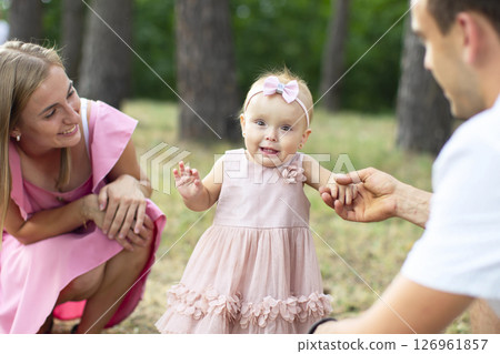 Husband, wife and their little daughter for a walk in the park. Happy dad and mom with one year old baby girl. Young family. 126961857