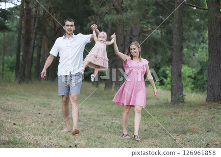Husband, wife and their little daughter for a walk in the park. Happy dad and mom throws up their little laughing one-year-old daughter. 126961858