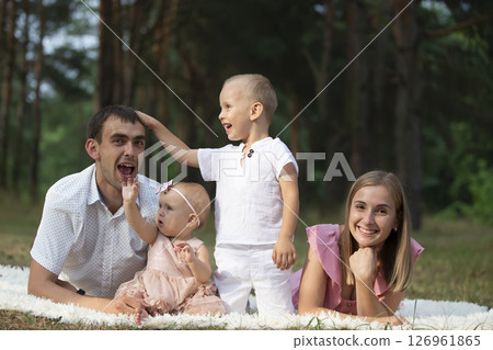 Husband and wife and their little children. Family portrait in nature. Mom and Dad with their brother and sister are lying on the grass. Young family with children for a walk. Husband and wife and their little children. Family portrait in nature. Mom and Dad with their brother and sister are lying on the grass. Young family with children for a walk. 126961865