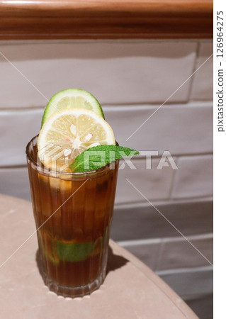 vertical photo of a glass of iced perfume lemon tea with lemon slice and a leaf placed on a table with white tile wall vertical photo of a glass of iced perfume lemon tea with lemon slice and a leaf placed on a table with white tile wall 126964275