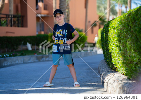 A young guy in a blue T-shirt stands on an alley near green bushes on the hotel grounds 126964391