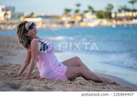 Woman sitting on the beach in a pink dress and enjoying her vacation 126964407