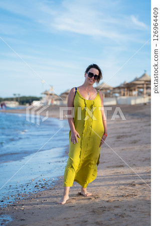 A woman in a yellow dress is standing on the beach 126964409