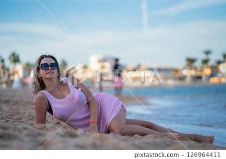 Woman lying on the beach near the sea in a pink dress and enjoying her vacati 126964411
