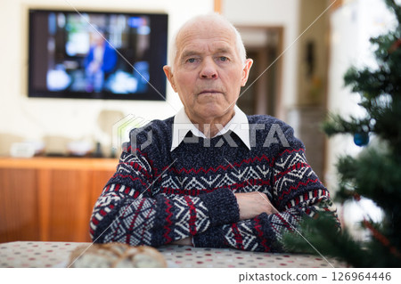 Bored elderly man sitting alone at table with small Christmas tree. 126964446