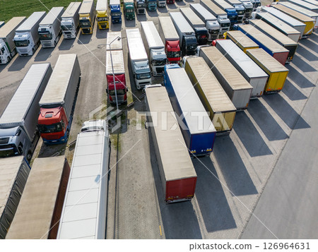 Aerial view of a large truck parking lot at a logistics hub, with multiple commercial semi trucks parked in organized rows. 126964631