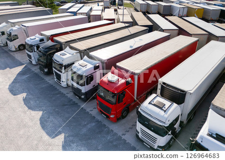 Aerial view of a large truck parking lot at a logistics hub, with multiple commercial semi trucks parked in organized rows. 126964683