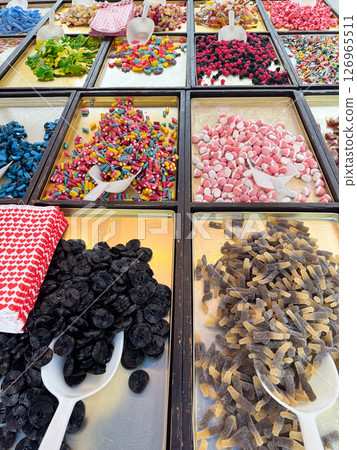 A vibrant assortment of various candies displayed in trays with plastic scoops. The image captures different shapes, textures, and colors, creating a feast for the eyes. 126965511