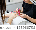A close-up view of a manicurist expertly applying vibrant red nail polish to a client's fingernails, illustrating the pampering and beauty ritual of a professional manicure 126966758