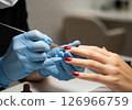 A close-up view of a manicurist expertly applying vibrant red nail polish to a client's fingernails, illustrating the pampering and beauty ritual of a professional manicure 126966759