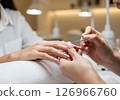 A close-up view of a manicurist expertly applying vibrant red nail polish to a client's fingernails, illustrating the pampering and beauty ritual of a professional manicure 126966760