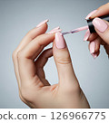 Close-up of a woman's hands meticulously applying vibrant red nail polish, showcasing the beauty and precision of a fresh manicure 126966775