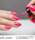 Close-up of a woman's hands meticulously applying vibrant red nail polish, showcasing the beauty and precision of a fresh manicure 126966777