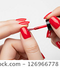 Close-up of a woman's hands meticulously applying vibrant red nail polish, showcasing the beauty and precision of a fresh manicure 126966778