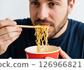 Close-up of a person slurping hot, steamy noodles directly from a bowl, showcasing the enjoyment of a quick and delicious meal. 126966821